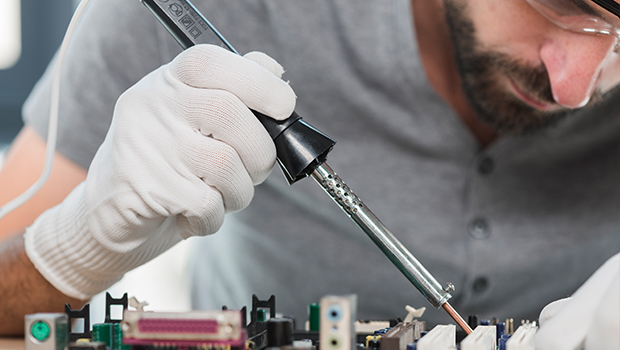 A man is sitting at a table, repairing a small coffee maker with a screwdriver. Close-up